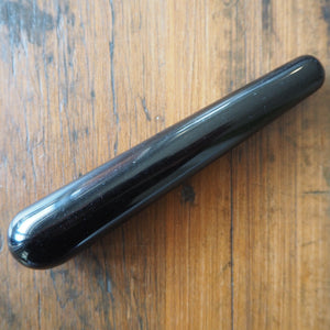 Small black obsidian yoni wand on wooden background